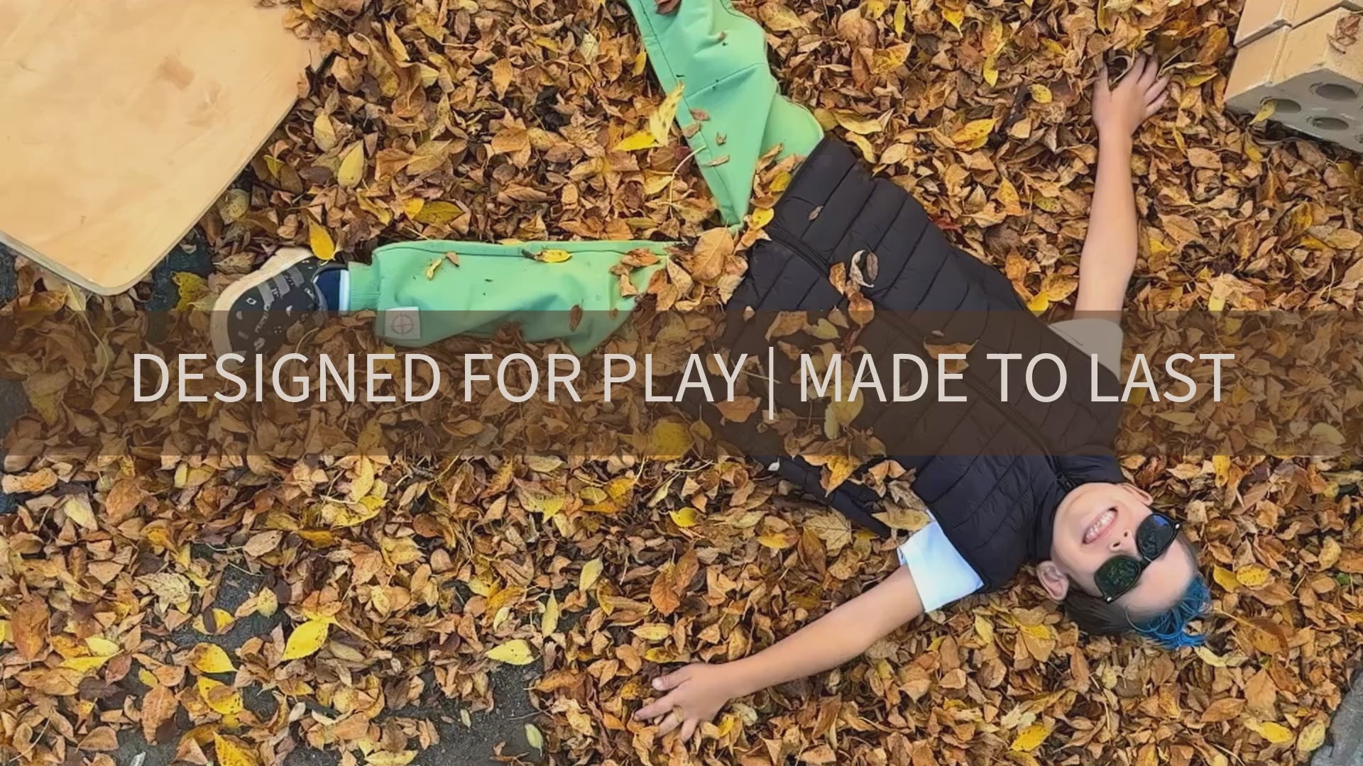 Load video: Two boys wearing green and brown colour jogger sets, playing the the fall leaves.